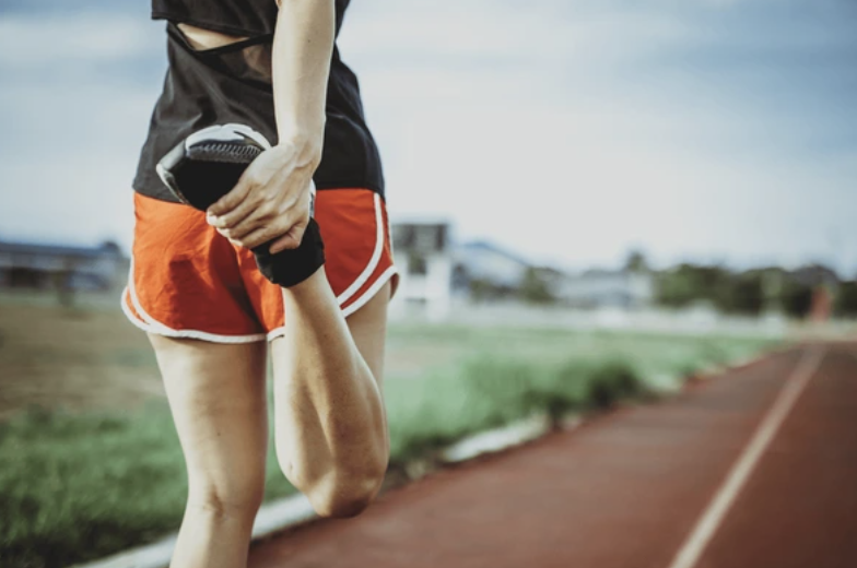 A woman performing stretching exercises in an outdoor setting, focusing on improving flexibility and preventing injury as part of a running routine.