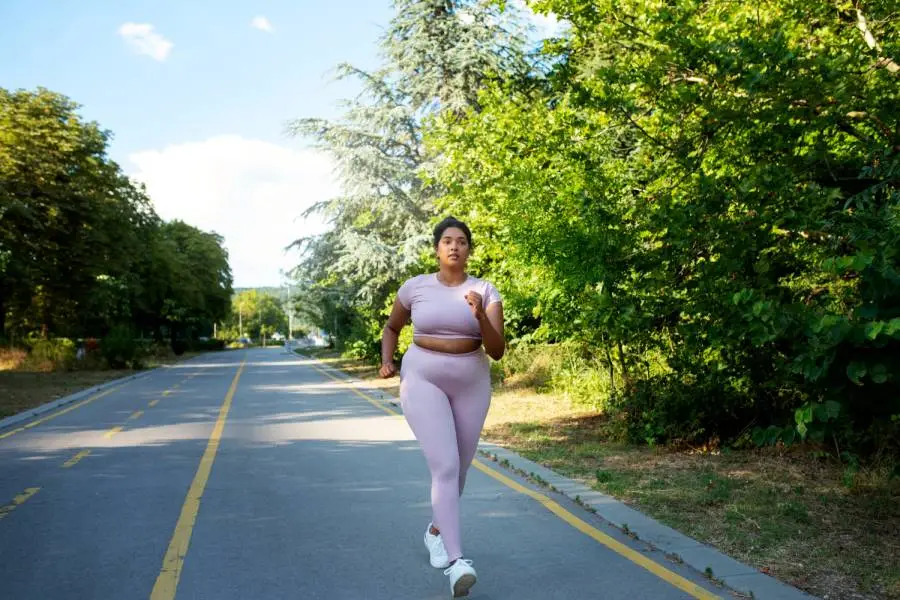 Woman running on a road, wearing athletic gear and focusing ahead.