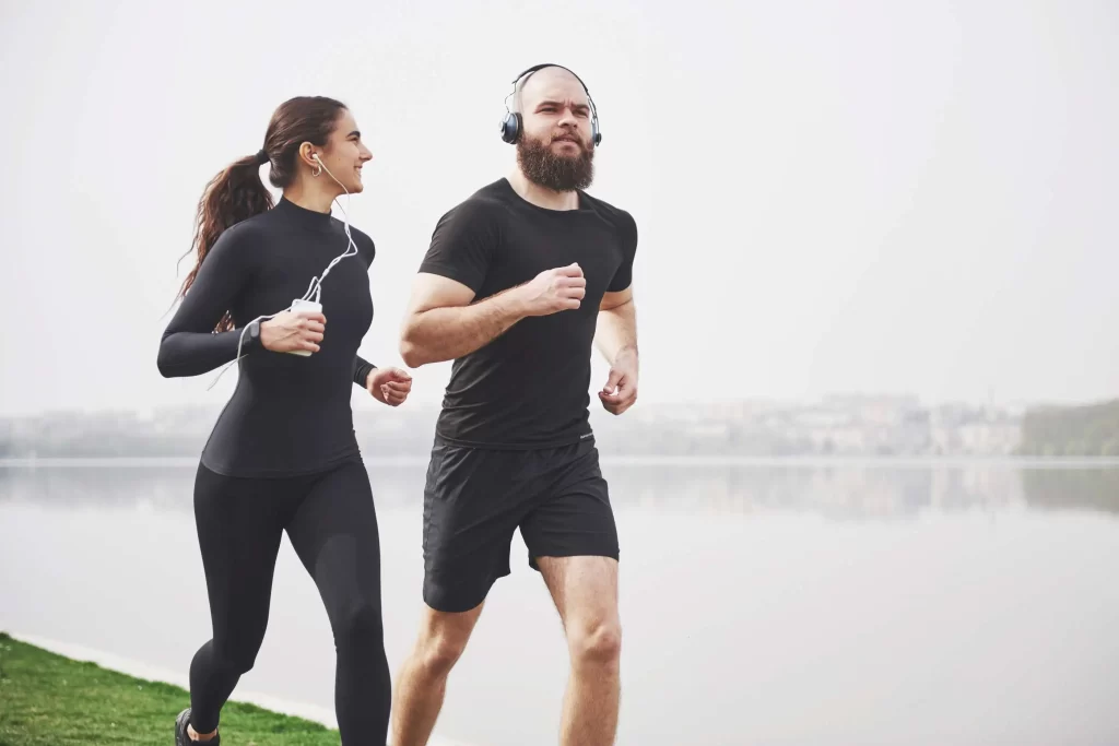 A couple jogging in the park, running side by side on a sunny day.